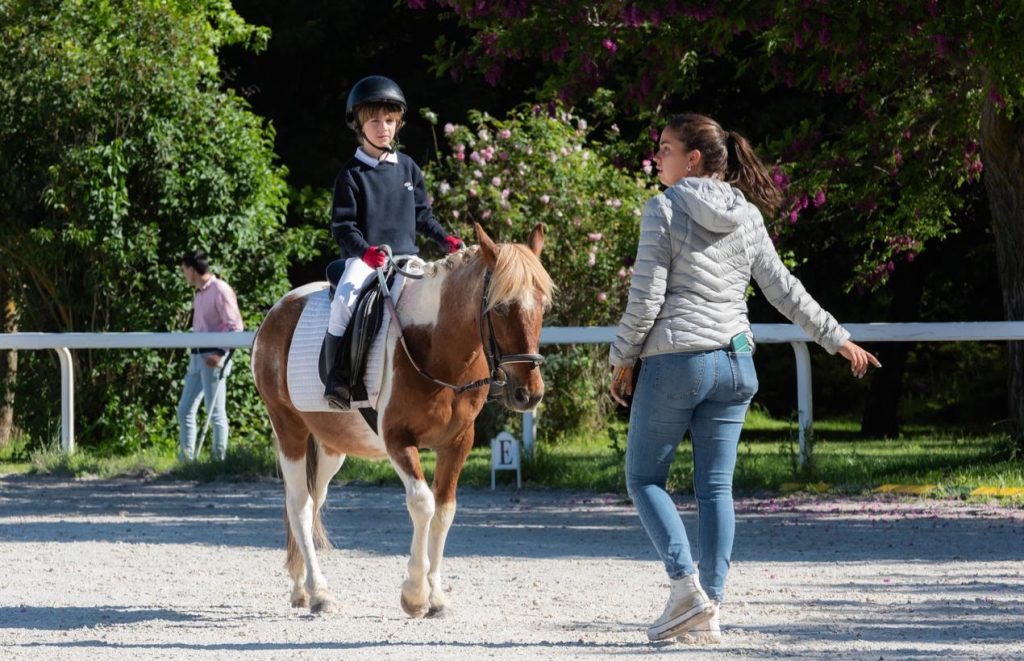 Niño montando un poni, acompañado por una instructora
