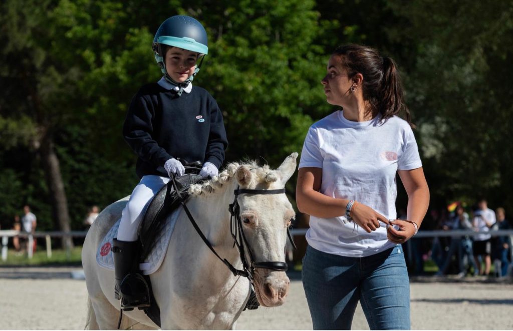 Niño montando en poni blanco mientras le acompaña una instructora